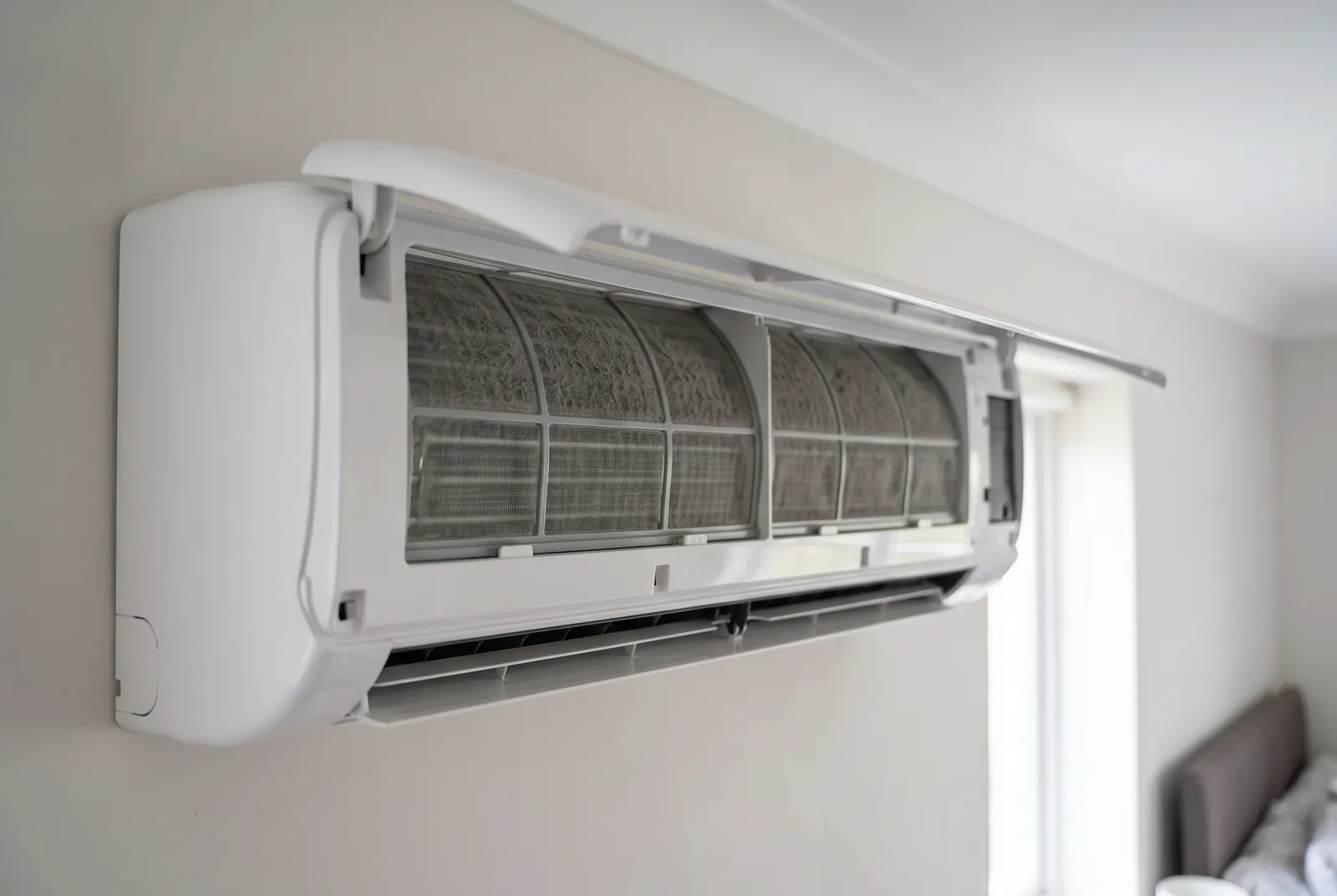 The front panel of a wall-mounted air conditioning unit lifted open, showing two mesh filters furred with grey dust